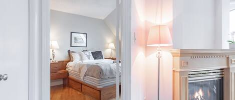 A bedroom with a bed, bedside tables, a nightstand, a fireplace, and a wall-mounted picture.