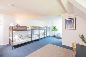 Ein Schlafraum mit Etagenbetten, einem blauen Teppich, einem Blumentopf und einem gerahmten Bild an der Wand.