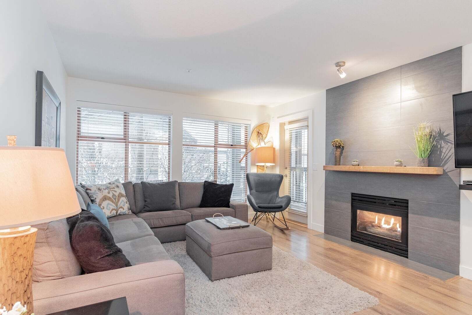 A modern living room with a sectional sofa, a small round table, a fireplace, and a television mounted on the wall.