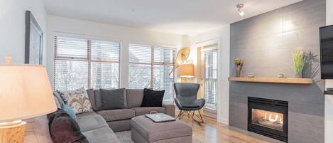 A modern living room with a sectional sofa, a small round table, a fireplace, and a television mounted on the wall.