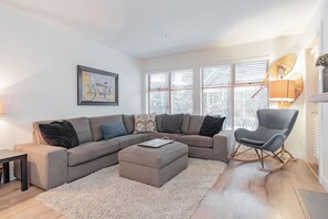 Ein modernes Wohnzimmer mit einem Ecksofa, einem Hocker und einem Schaukelstuhl.