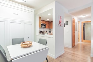 Eine moderne Küche mit Holzschränken, einer weißen Arbeitsplatte und einem Essbereich mit weißem Tisch und grauen Stühlen.