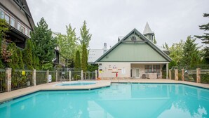 Una piscina con área cercada, un edificio con techo verde y árboles al fondo.