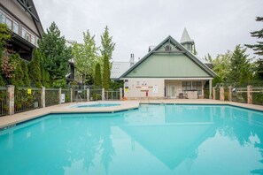 Ein Swimmingpool mit Umzäunung, ein Gebäude mit Gründach und Bäume im Hintergrund.