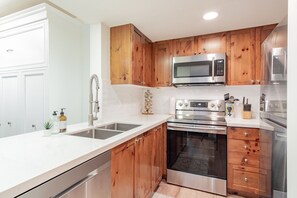 Eine moderne Küche mit Holzschränken, Edelstahlgeräten und einer weißen Arbeitsplatte.
