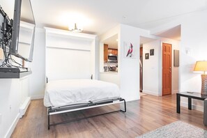 Ein gemütliches Schlafzimmer mit einem Bett, einem Schreibtisch und einer kleinen Küche im Hintergrund.