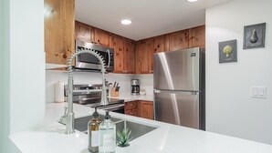 Una cocina moderna con electrodomésticos de acero inoxidable, armarios de madera y encimera blanca.