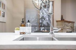 A kitchen with a modern faucet, two soap bottles labeled 'Dish Soap' and 'Hand Soap,' and a small potted plant on the counter. - Pool & hot tub | Free parking | Excellent location (Whistler)