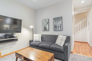 A modern living room with a grey sofa, a wooden coffee table, a flat-screen TV, and two framed pictures on the wall. - Pool & hot tub | Free parking | Excellent location (Whistler)