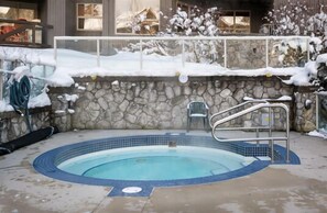 A swimming pool with a stone wall, metal ladder, and a chair. - Ski-in/out apartment | Shared Hot Tub, Pool & Gym | Superb location (Whistler)