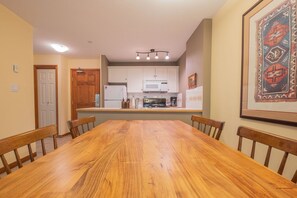 Une salle à manger avec une table et des chaises en bois, une cuisine avec des meubles blancs et un tapis encadré accroché au mur.