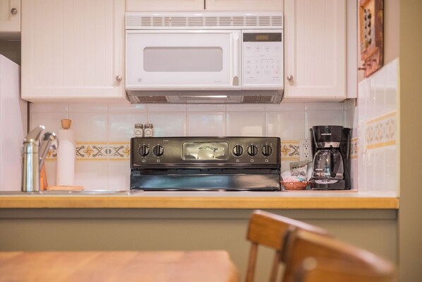 A kitchen with a white microwave, a black stove, and a coffee maker on the counter. - Ski-in/out apartment | Shared Hot Tub, Pool & Gym | Superb location (Whistler)