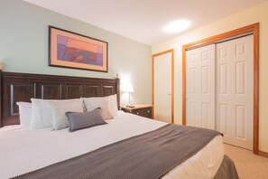 A neatly made bed with a headboard, a bedside lamp, and a framed picture on the wall. - Ski-in/out apartment | Shared Hot Tub, Pool & Gym | Superb location (Whistler)