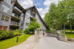 Un immeuble résidentiel à plusieurs étages, doté de balcons, d’une allée sinueuse et d’un espace verdoyant avec des arbres.
