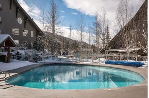 A swimming pool surrounded by buildings with a snowy landscape in the background. - Ski-in/out apartment | Shared Hot Tub, Pool & Gym | Superb location (Whistler)