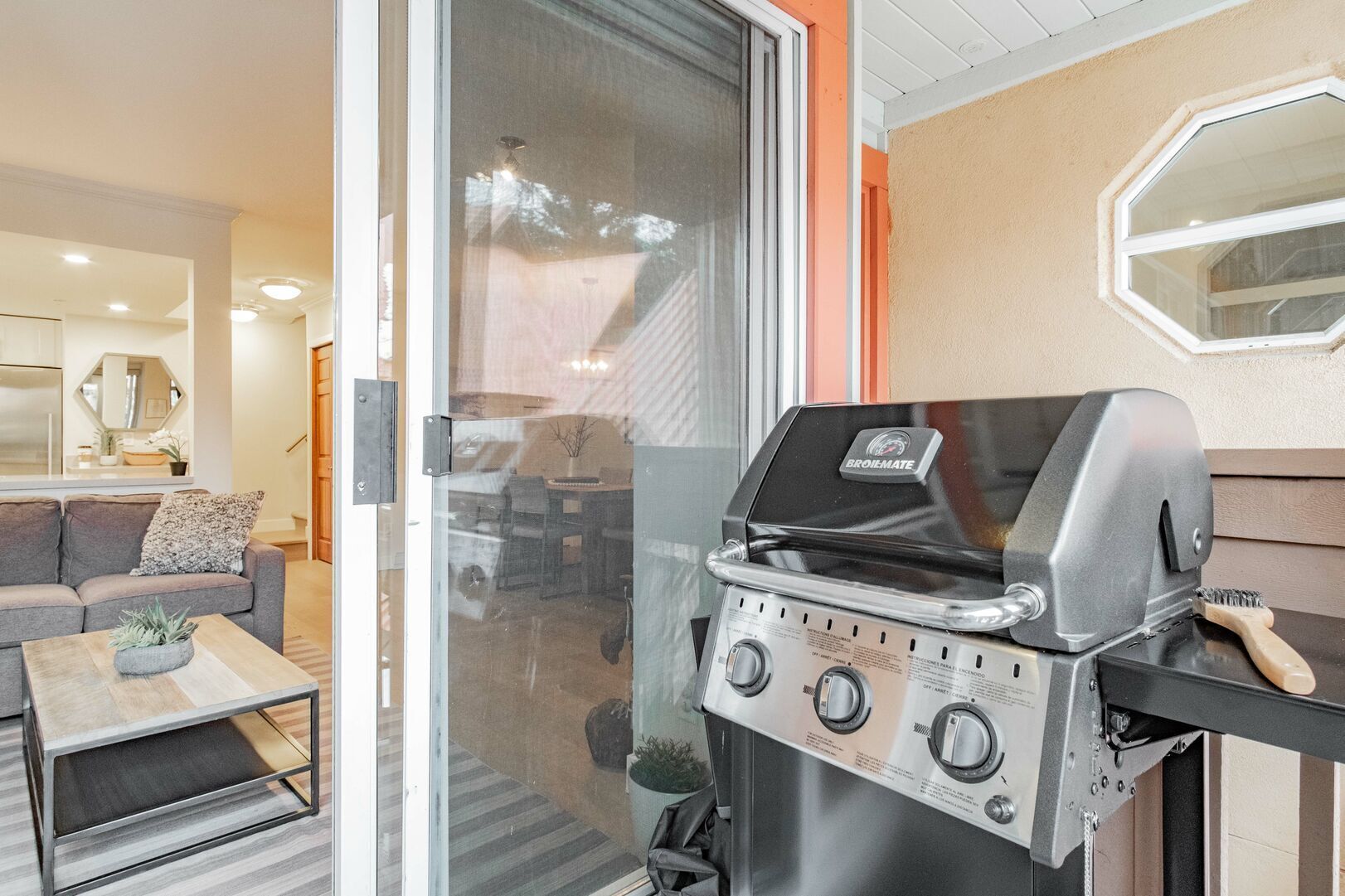 A modern kitchen with a built-in grill, a glass door leading to a living area, and a small table with a plant.
