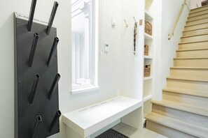 Moderni sisustus, jossa on valkoinen penkki, puinen portaikko ja metallinen hylly koukuilla.