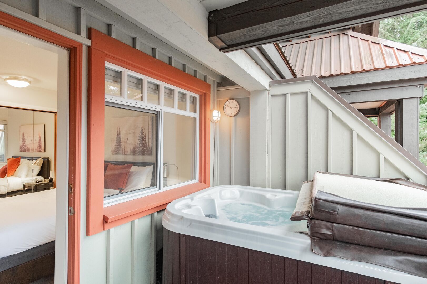 A hot tub with a wooden exterior, a window with a red frame, and a staircase leading to an upper level.