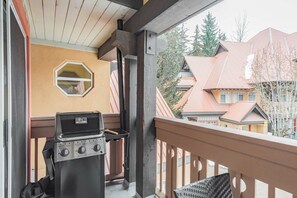 Ein Balkon mit Grill, einem Fenster und Blick auf benachbarte Häuser.