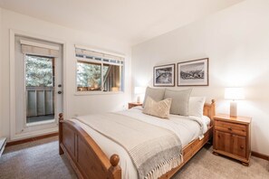 A bedroom with a wooden bed, two bedside tables with lamps, a door with a view, and two framed pictures on the wall. - Central location | Pets | BBQ | Free parking (Whistler)