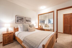 Une chambre à coucher avec un lit en bois, une table de chevet avec une lampe, un grand miroir et deux tableaux encadrés accrochés au mur.
