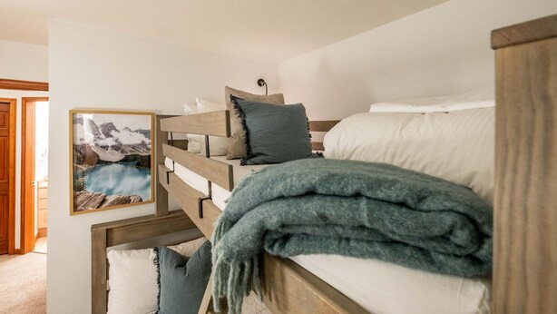 Een slaapkamer met stapelbed, een lijst met een berglandschap, een houten hoofdbord en een blauwe deken.