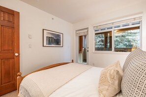 A bedroom with a bed, a window with a view of trees, a door, and a framed picture on the wall. - Central location | Pets | BBQ | Free parking (Whistler)