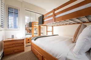 Quarto com beliche, cabeceira de madeira, mesa de cabeceira com abajur e guarda-roupa com porta de correr.