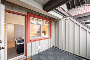 Ein Zimmer mit einem Bett, einem Fenster mit Jalousien, einer Tür und einem kleinen Außenbereich mit einer Holzterrasse.