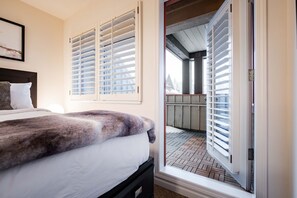 Ein Schlafzimmer mit Bett, einem Fenster mit Jalousien und Blick auf eine Terrassenanlage.