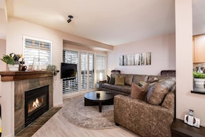 A living room with a fireplace, a sofa, a coffee table, and a TV. - Excellent location | Renovated | Pool & hot tub | BBQ (Whistler)