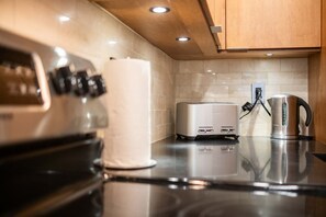 A kitchen with a stove, a toaster, and a kettle on the counter. - Excellent location | Renovated | Pool & hot tub | BBQ (Whistler)