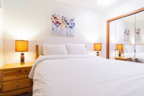 A hotel room with a bed, two bedside tables with lamps, a wooden dresser, and a large mirror. - Beautiful Townhome in Whistler Centre, Pets, BBQ (Whistler)
