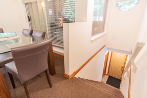 Eine Treppe mit hölzernem Geländer, ein Glastisch mit Stühlen und eine Tür am Fußende.