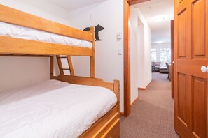 Ein Stockbett mit einer Leiter, eine Holztür und ein Flur, der in einen anderen Raum führt.