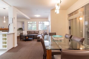 A spacious living room with a glass dining table, leather sofas, and a kitchen area with a countertop and sink. - Beautiful Townhome in Whistler Centre, Pets, BBQ (Whistler)