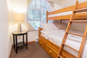 Ein Etagenbett mit einer Leiter, ein Nachttisch mit einer Lampe und ein Fenster mit Jalousien.