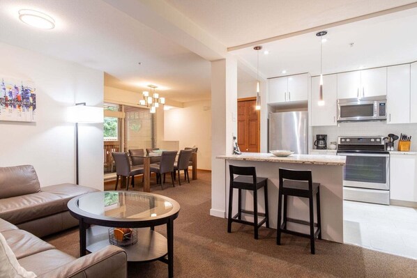 A modern kitchen with stainless steel appliances, a dining area with a glass table, and a living space with a leather sofa. - Beautiful Townhome in Whistler Centre, Pets, BBQ (Whistler)