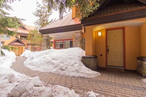 A snow-covered pathway leading to a building with a stone pillar and a door. - Beautiful Townhome in Whistler Centre, Pets, BBQ (Whistler)