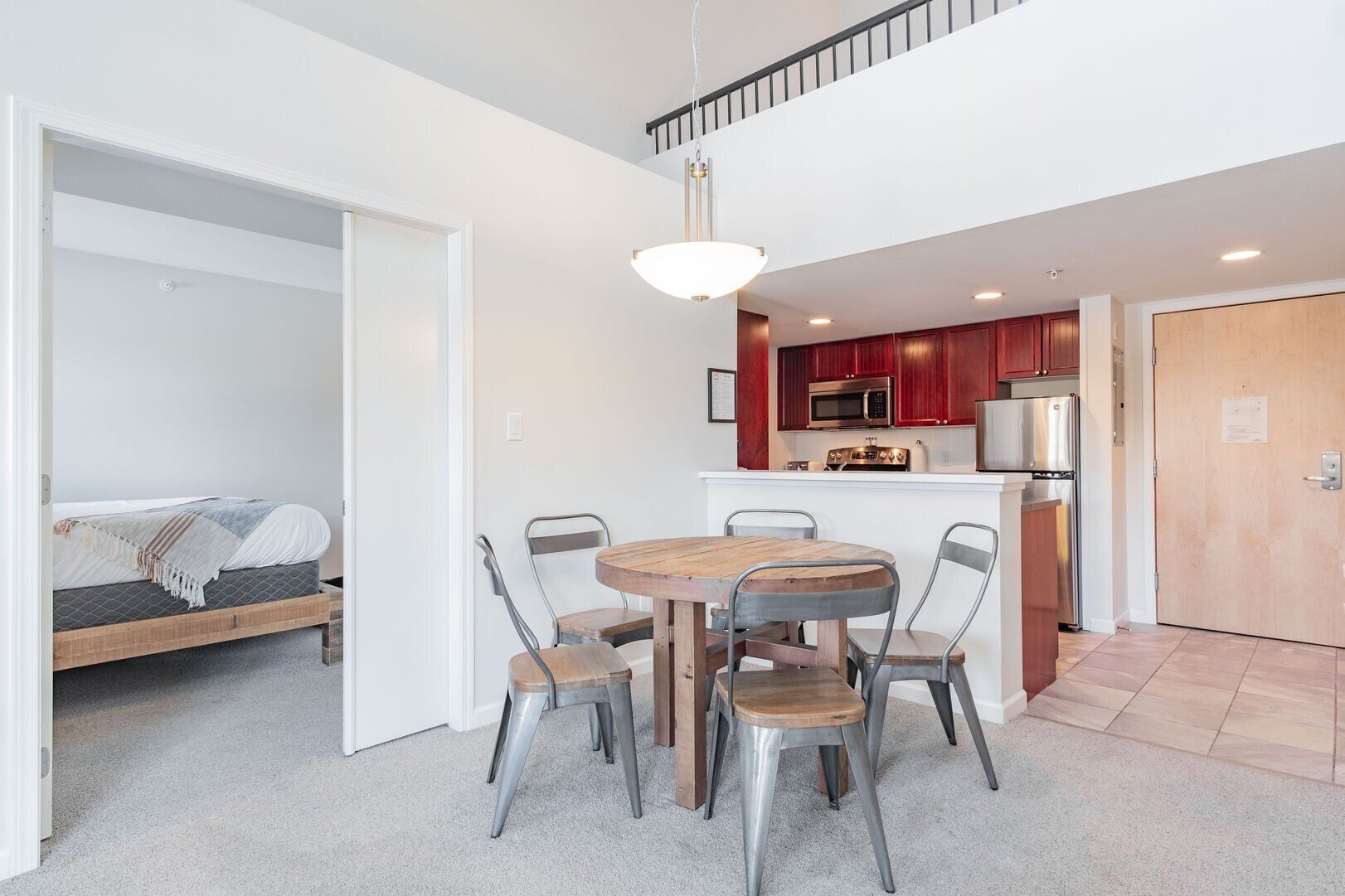 A modern apartment with a dining area, kitchenette, and a bedroom.