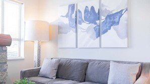 En grå soffa med mönstrade kuddar, en abstrakt målning som hänger på väggen, en lampa och en vägg av sten.