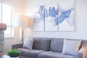 A grey sofa with patterned cushions, a wall-mounted abstract painting, a lamp, and a stone wall. - Village location| Pool & hot tub | Free parking (Whistler)