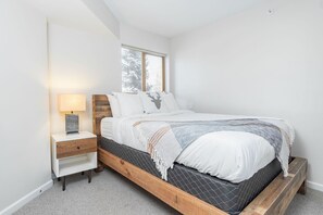 A bedroom with a bed, bedside table, lamp, and window. - Village location| Pool & hot tub | Free parking (Whistler)