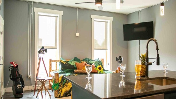 A modern kitchen with a central island, a flat-screen TV mounted on the wall, and a seating area with a sofa and a tripod.