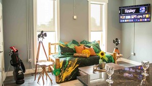 A room with a green sofa, a tripod, a golf bag, and a TV displaying 'Friday'.