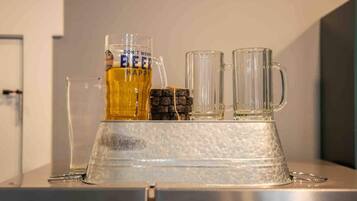 Un espace bar avec un grand verre à bière, deux verres transparents et une bouteille de bière posés sur un comptoir métallique.