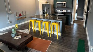 A modern kitchen with a central island, bar stools, and a dining area with a coffee table.