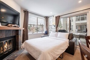 A hotel room with a bed, a fireplace, a TV, and large windows. - Free parking | Hot tub | Steps to Blackcomb (Whistler)