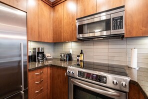 A modern kitchen with stainless steel appliances, wooden cabinets, and a granite countertop. - Free parking | Hot tub | Steps to Blackcomb (Whistler)