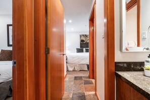 A hotel room with a bed, a bathroom with a mirror and sink, and a hallway with wooden doors. - Free parking | Hot tub | Steps to Blackcomb (Whistler)